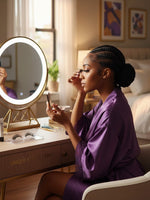 Woman in purple robe applying Unique Style 2 Envy Inc Chloe 3D mink strip lashes in front of a lighted vanity mirror.